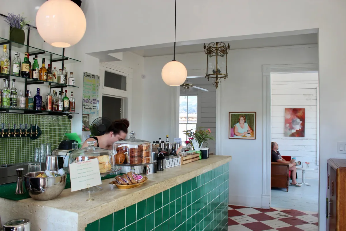 Green-tiled bar counter with bottle shelves, pendant lamps and a barista in a bright white converted house