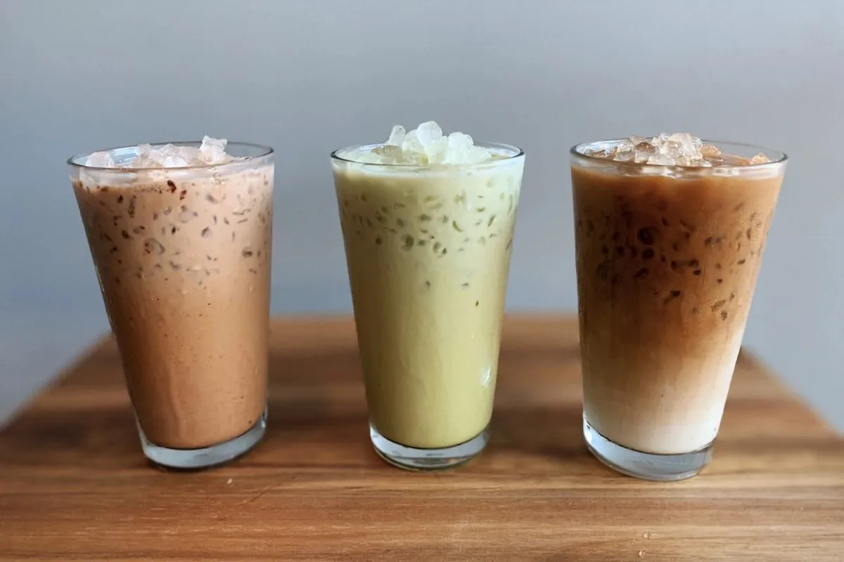 Three iced coffee and matcha drinks in clear cups lined up on a wooden board