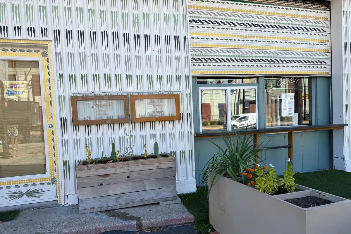 Storefront painted in white and gold patterns, with planters of succulents and flowers by the walk-up window