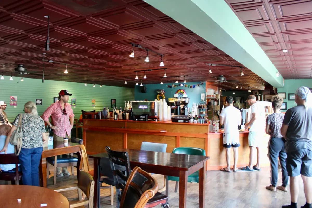 Customers queue at a wooden counter under a red pressed-tin ceiling with mismatched tables in the foreground