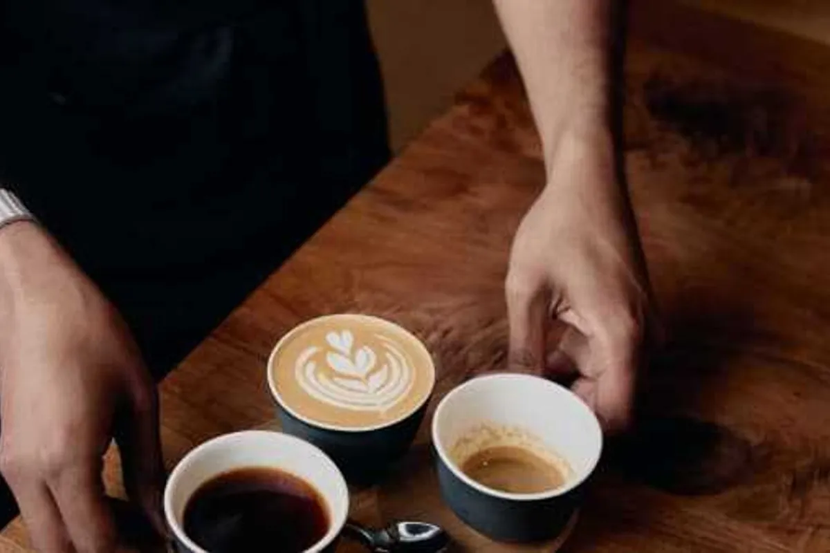Hands setting down a latte-art flat white and two espressos on a wooden table