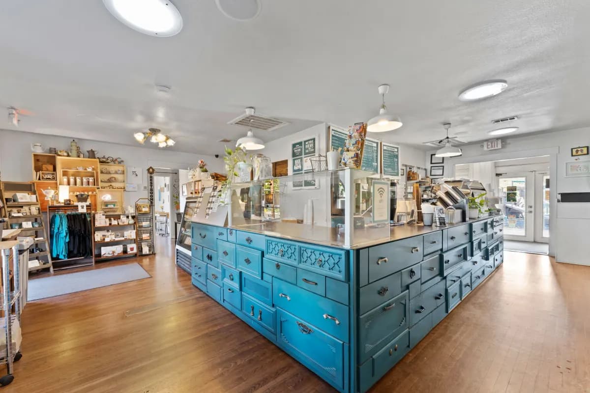 Main room with a teal drawer-front counter, retail shelves and wood floors in bright daylight