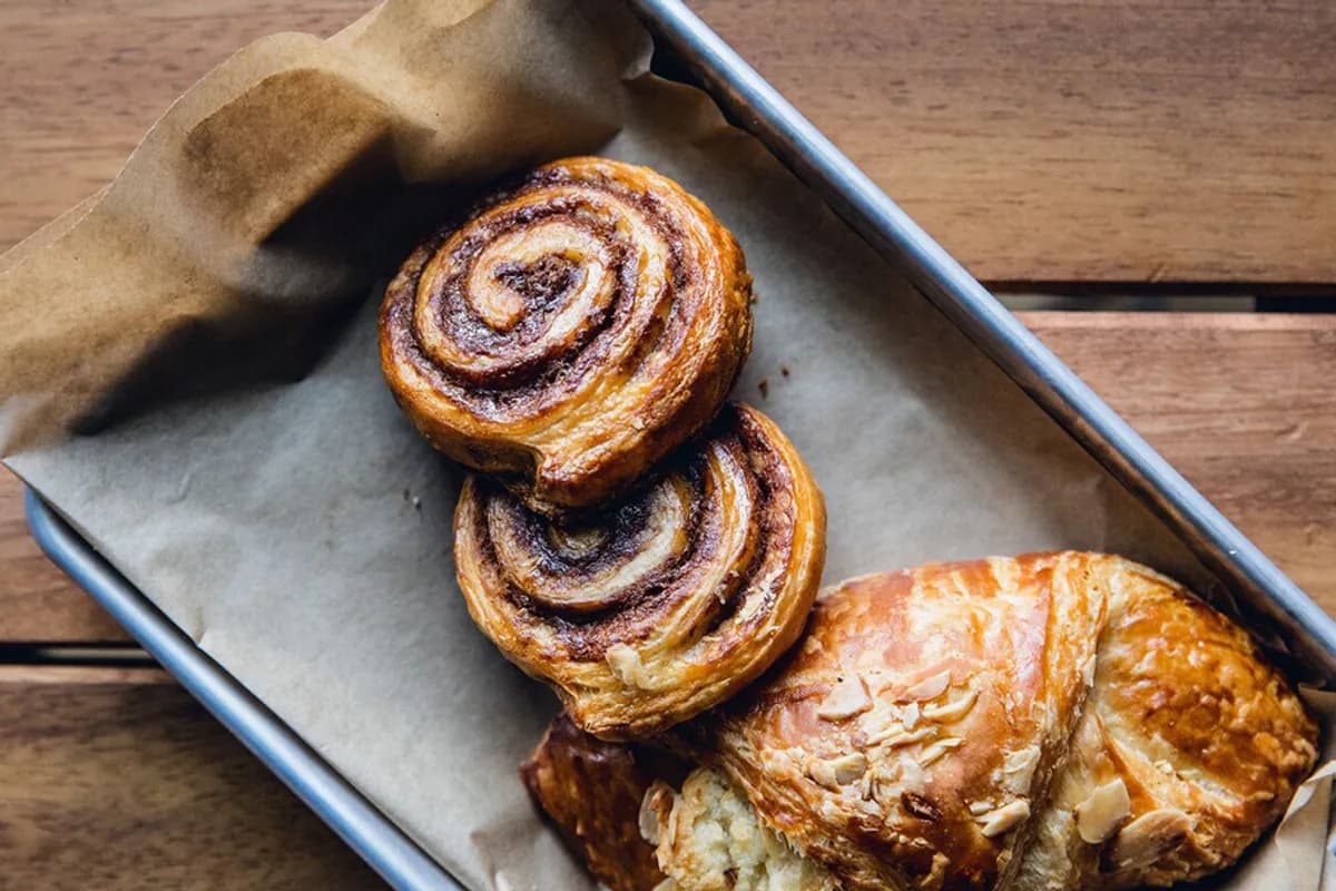 Overhead of cinnamon swirl rolls and an almond croissant on parchment in a metal tray on wood