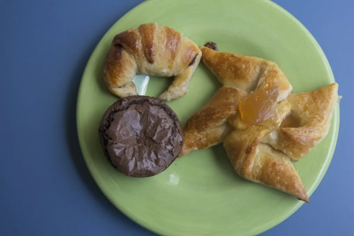 Croissant, brownie and fruit danish pinwheel pastries on a green plate against a blue table