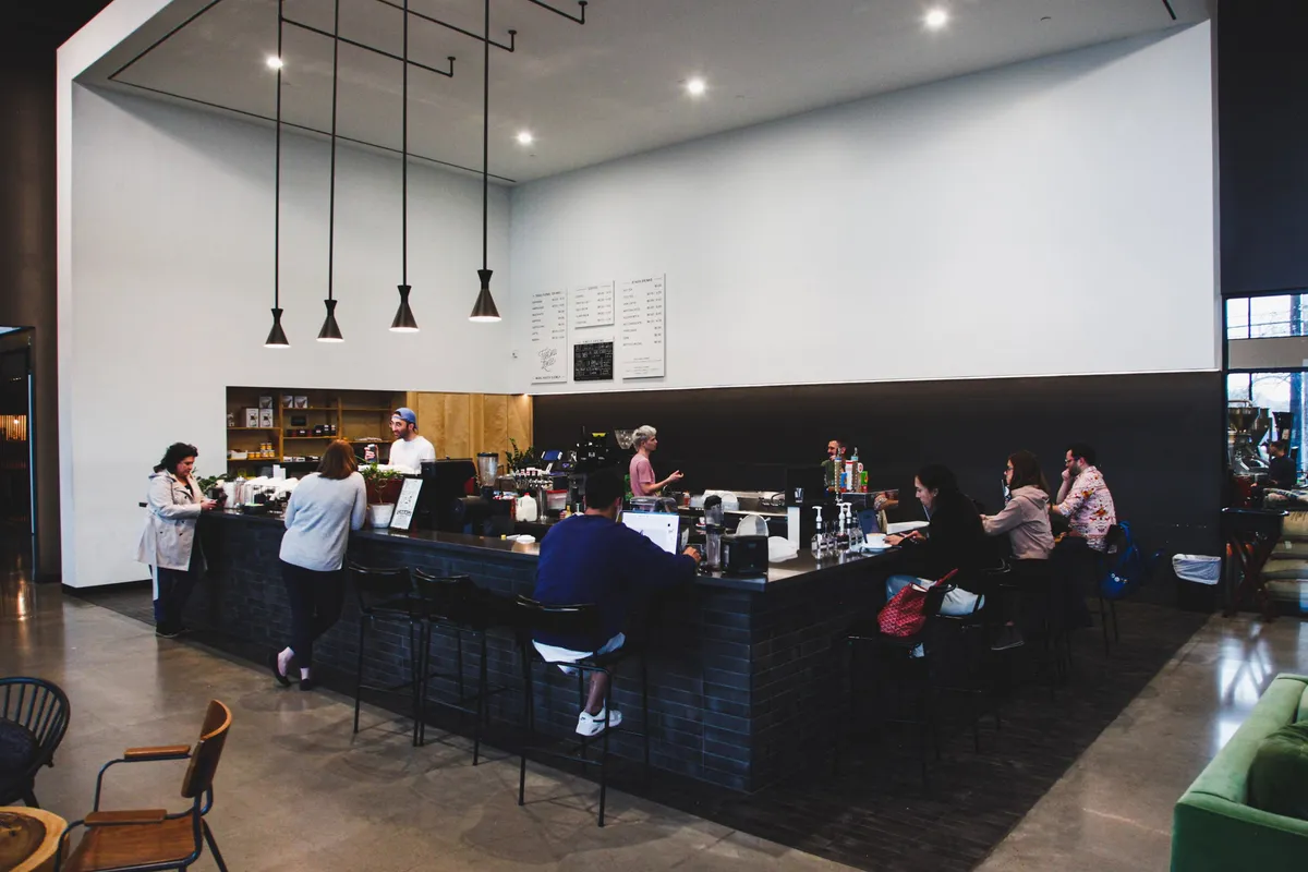 A long dark-tiled espresso bar under hanging pendant lights, regulars on stools at the Springdale cafe