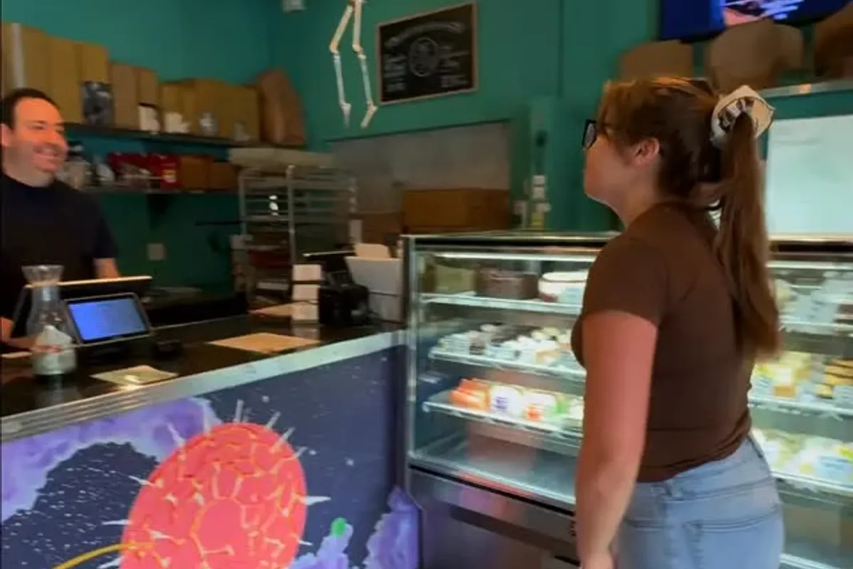 Customer browsing the bakery case inside the teal-walled coffeehouse with a mosaic counter front