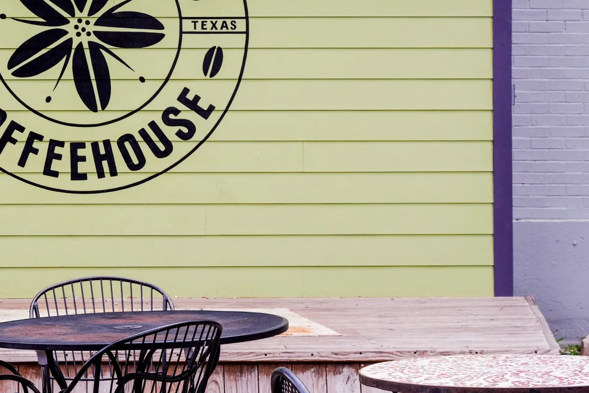 Cherrywood Coffeehouse patio with iron bistro tables and striped umbrella before a green wall bearing the coffeehouse logo