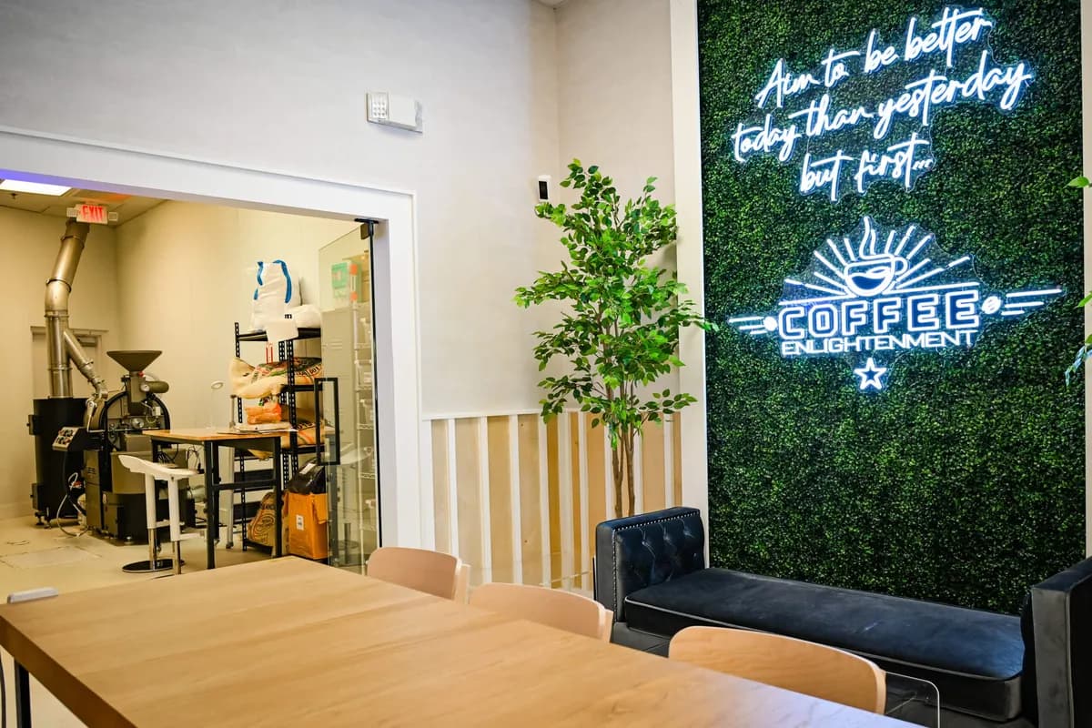 Coffee Enlightenment dining room with neon sign on green wall, wood table, and glimpse of the roasting room