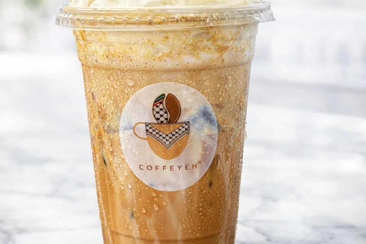 Iced Coffeyeh frappe topped with whipped cream in a branded cup against a marble table and soft window light