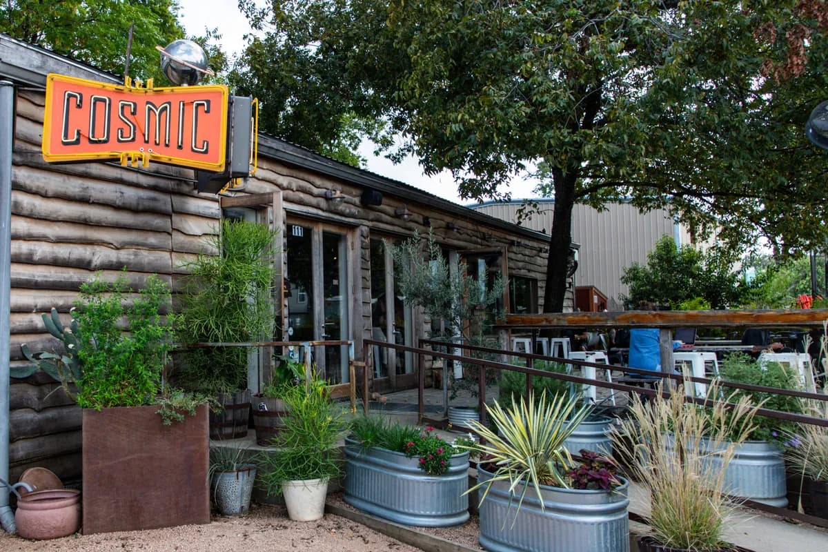 Log-cabin style Cosmic Coffee building with neon sign, tree shade and landscaped planters on Pickle Road