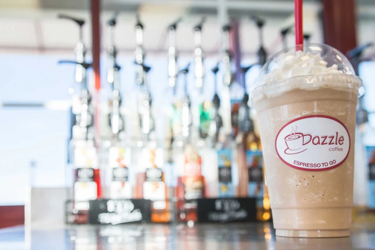 Dazzle Coffee blended iced drink with whipped cream in front of a row of flavor syrup bottles