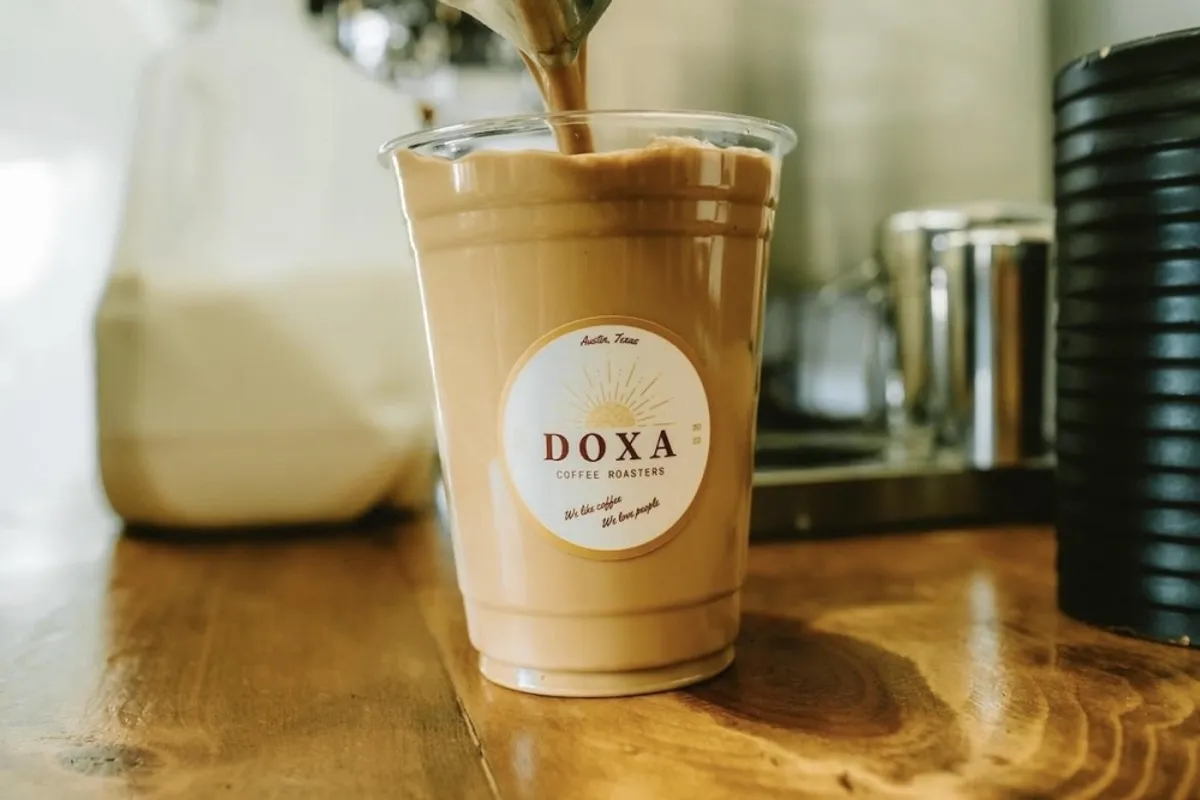 Doxa Coffee Roasters iced latte with logo sticker on a wooden counter as espresso is poured in