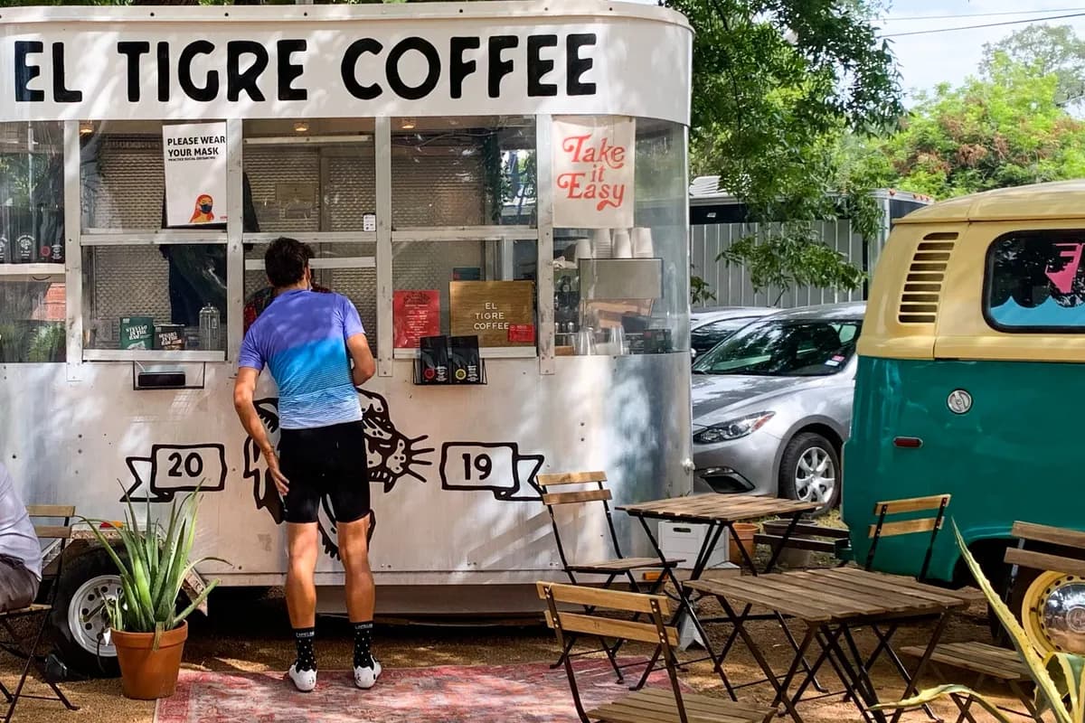 El Tigre Coffee white trailer with serving window, shaded yard seating and customers beside a teal vintage van
