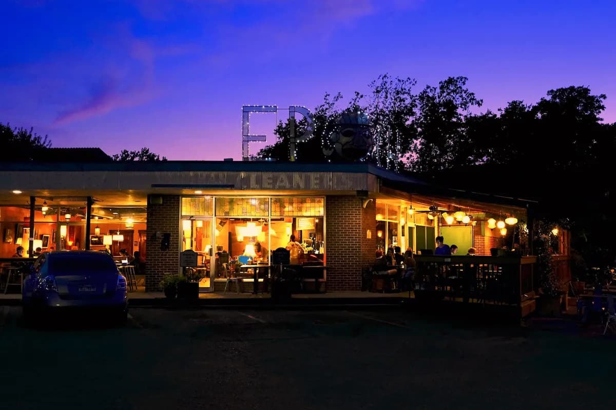Lit-up coffeehouse storefront and patio glowing at dusk under a purple sky with the Epoch sign lettering
