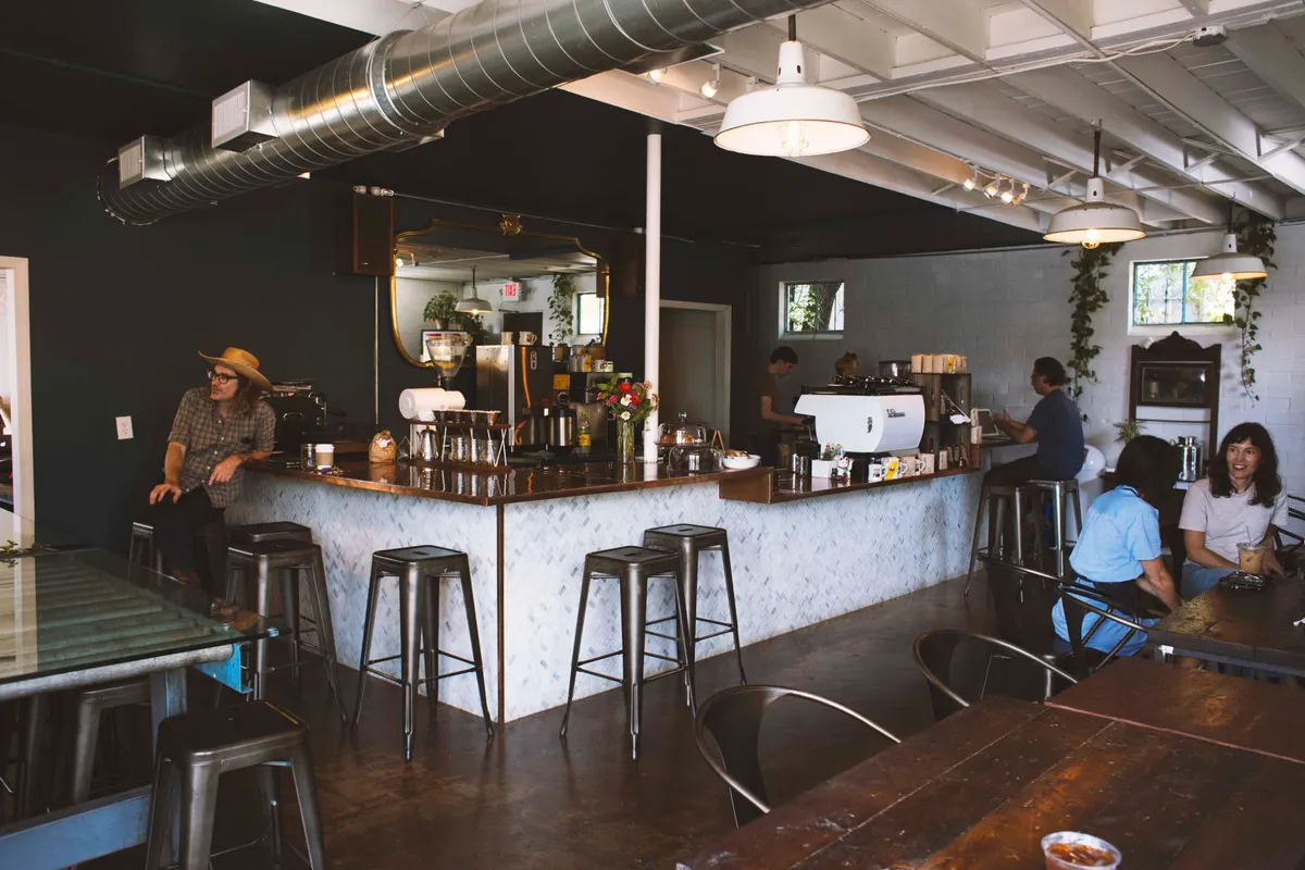 Interior with white tiled bar, metal stools, pendant lamps and customers chatting at the counter under a dark ceiling