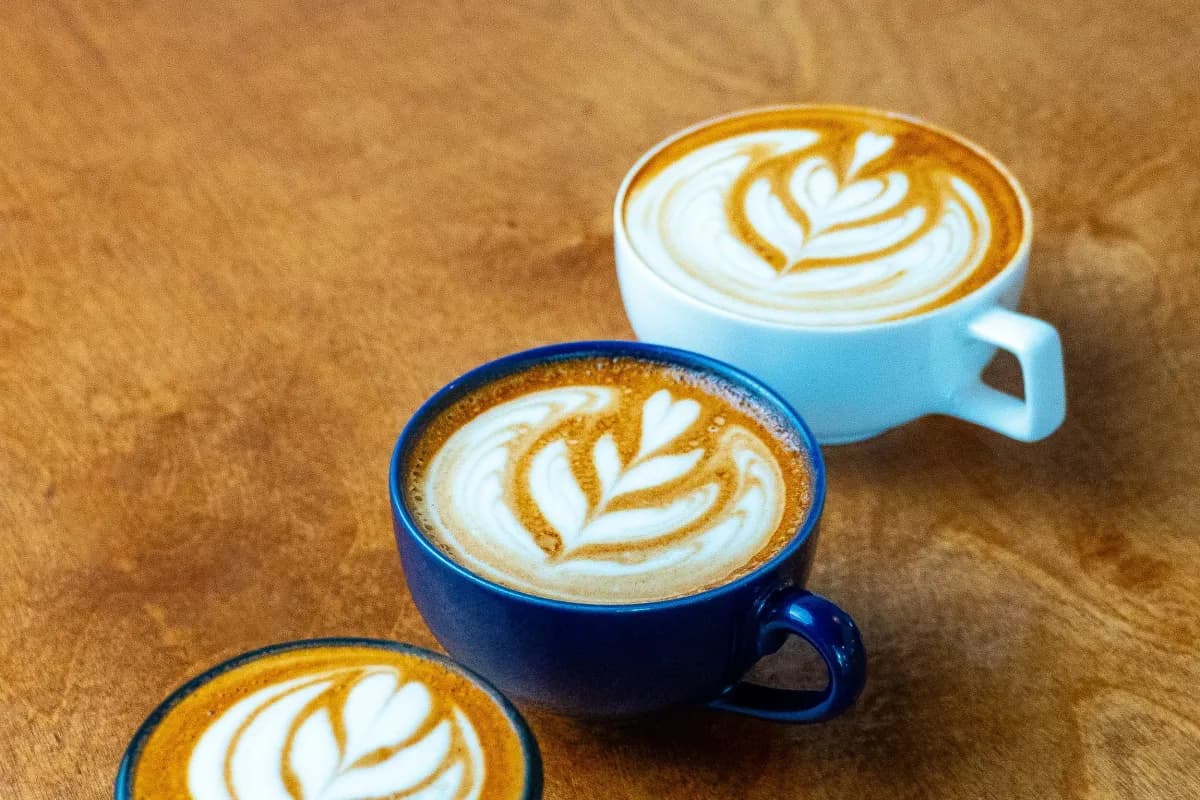 Three lattes with leaf latte art in blue and black cups on a wooden table