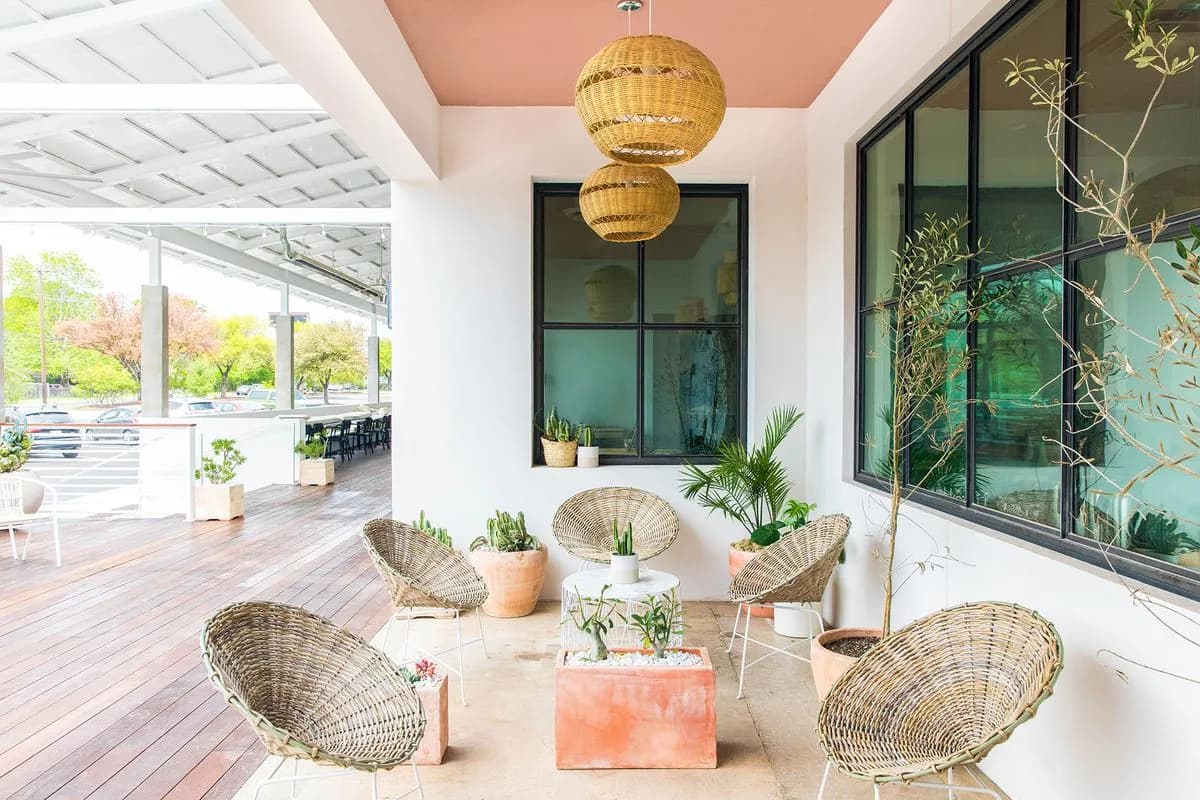 Covered patio with wicker chairs, rattan pendant lamps, potted cacti and a pink ceiling beside large windows