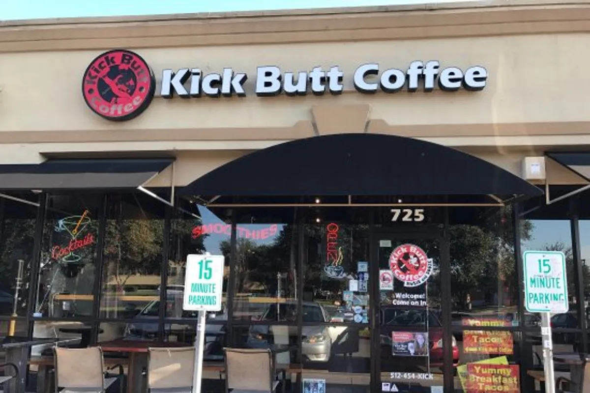 Kick Butt Coffee storefront in a strip center with black awning, sign and patio chairs
