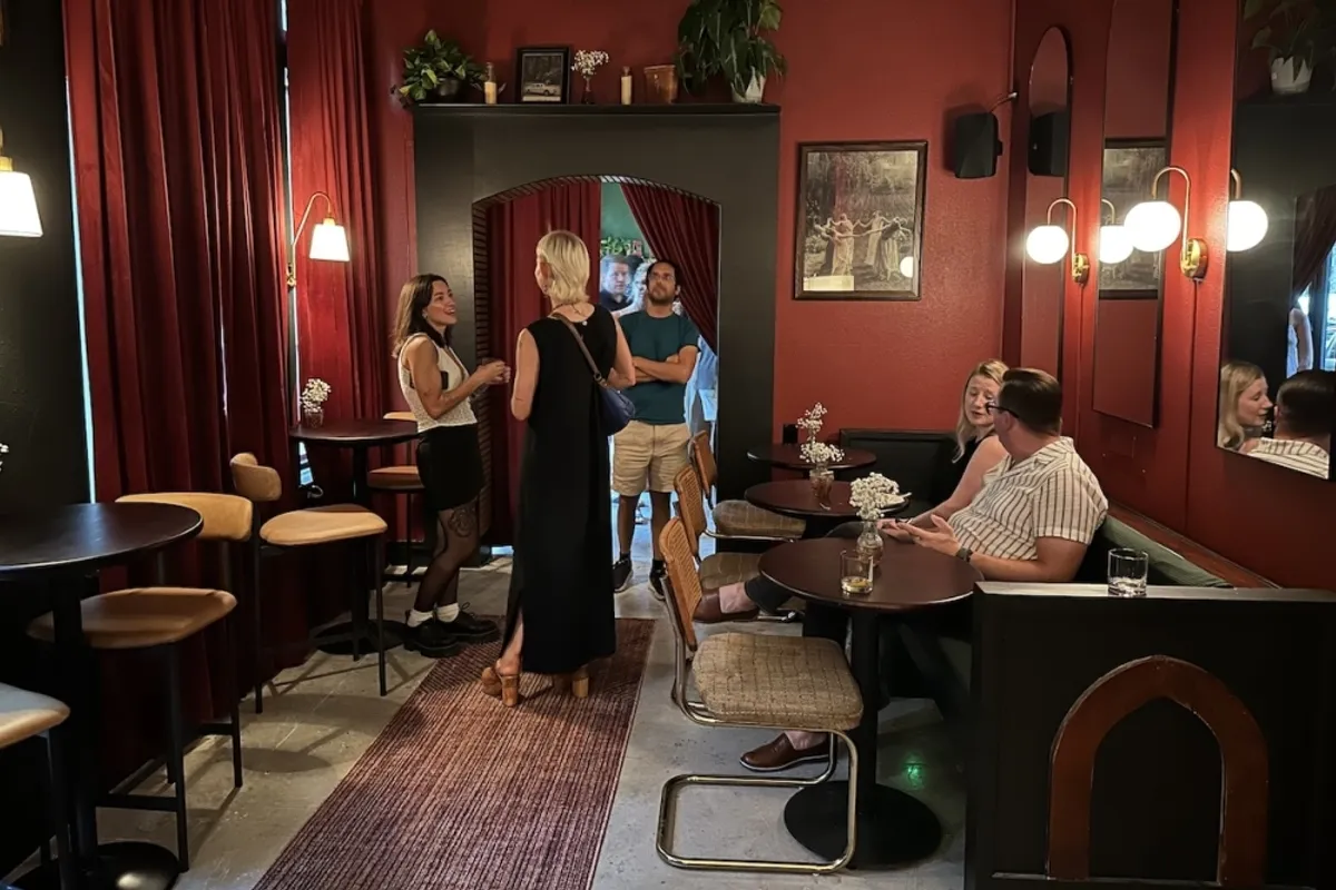 Red-walled cafe room with velvet curtains, bistro tables, cane chairs and guests chatting under an arched doorway