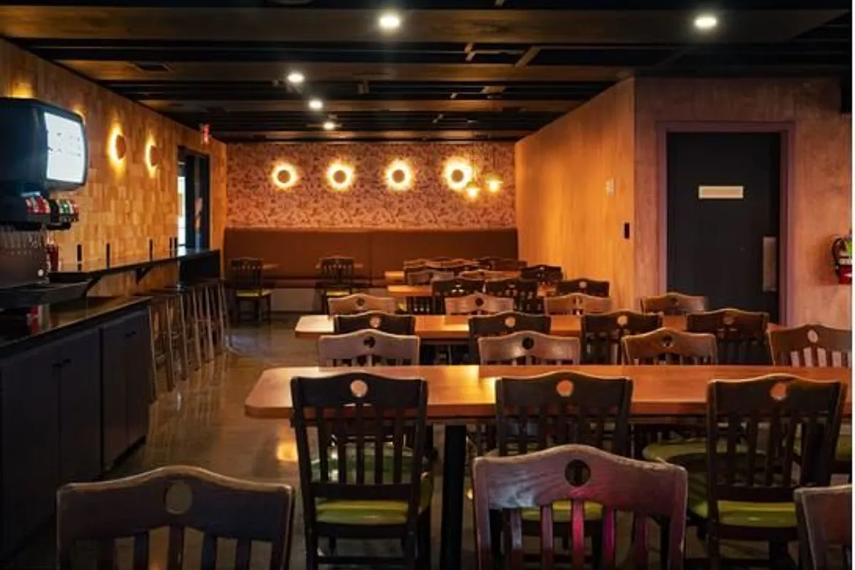 Dining room with wooden chairs and tables, glowing round wall lights and a patterned banquette