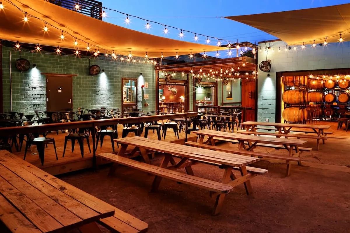 Lazarus Brewing patio at dusk with string lights, picnic tables, shade sails and barrels in the taproom