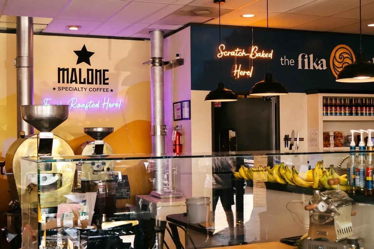Malone Specialty Coffee interior with brass roasters, neon sign and pastry counter with bananas