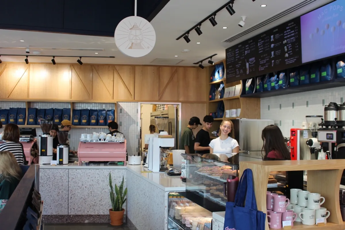Merit Coffee counter with pink espresso machine, wood paneling, coffee bags on shelves and baristas at work