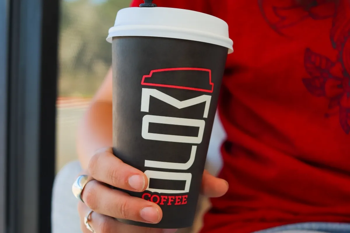 Hand holding a black Mojo Coffee paper cup with white lid in front of a window