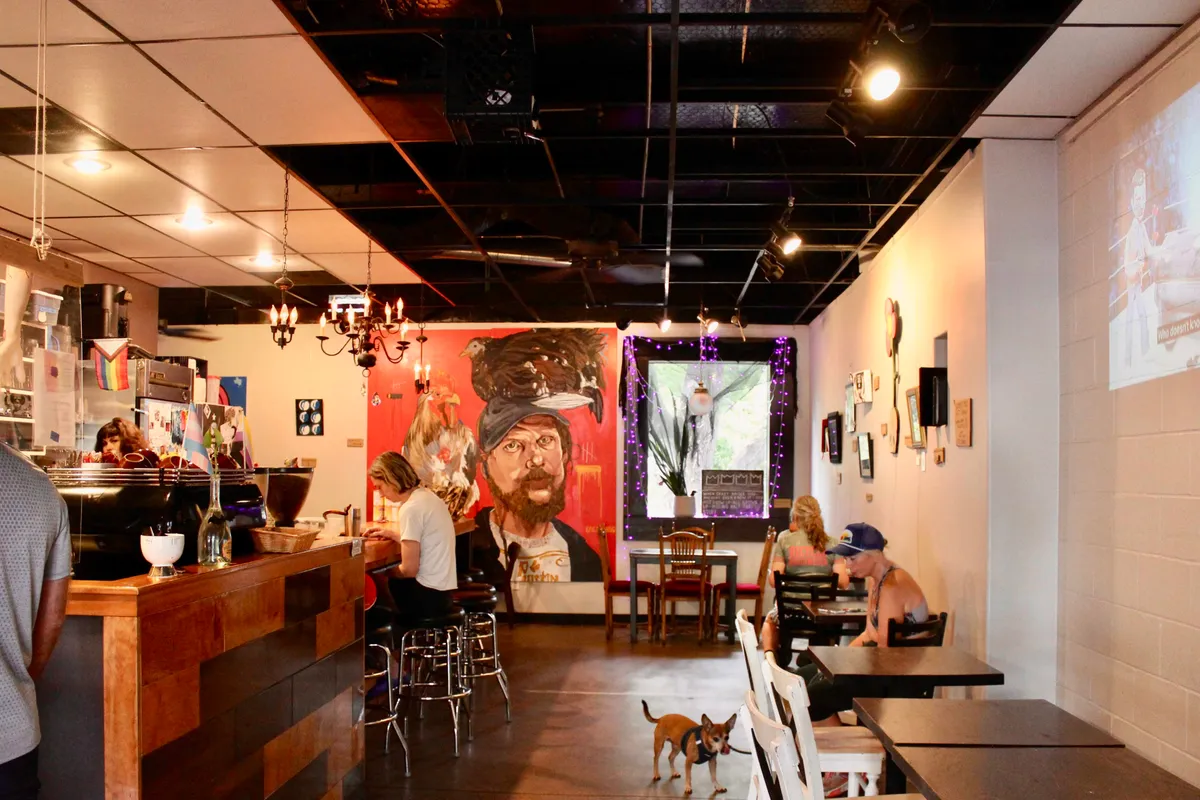 Wood-front counter with stools at left, red portrait mural and tables beneath a black ceiling at Once Over Coffee Bar