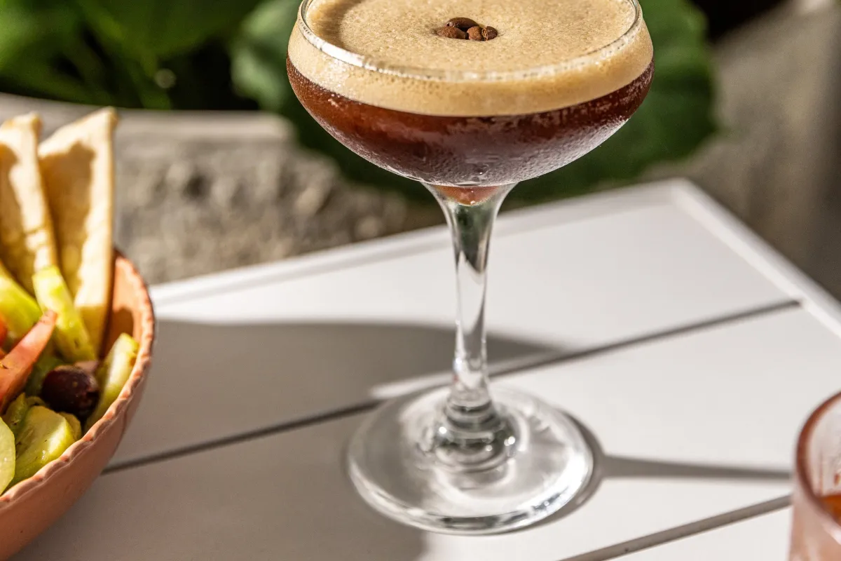 An espresso martini in a coupe glass with coffee beans on a candlelit tray at OPA, tropical leaves behind