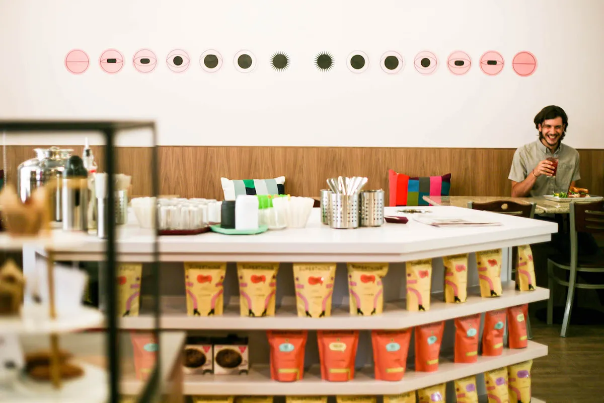 Patika Luncheonette island counter stacked with orange coffee bags, a diner at the far end beneath a row of pink dots