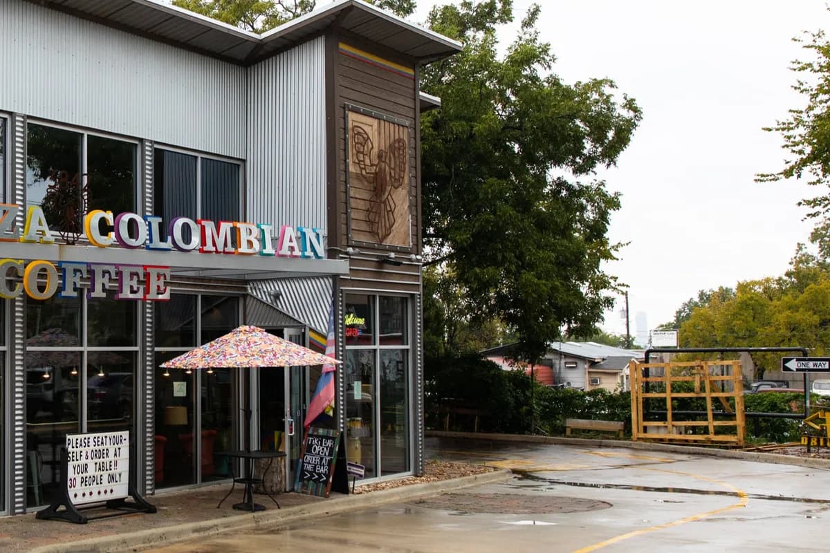 Plaza Colombian Coffee building exterior with multicolor lettered sign, glass front and patio umbrella among trees