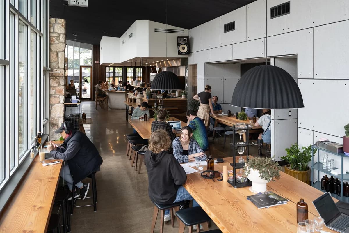 Bright Proud Mary cafe interior with long communal table, tall windows and baristas at the bar in the back