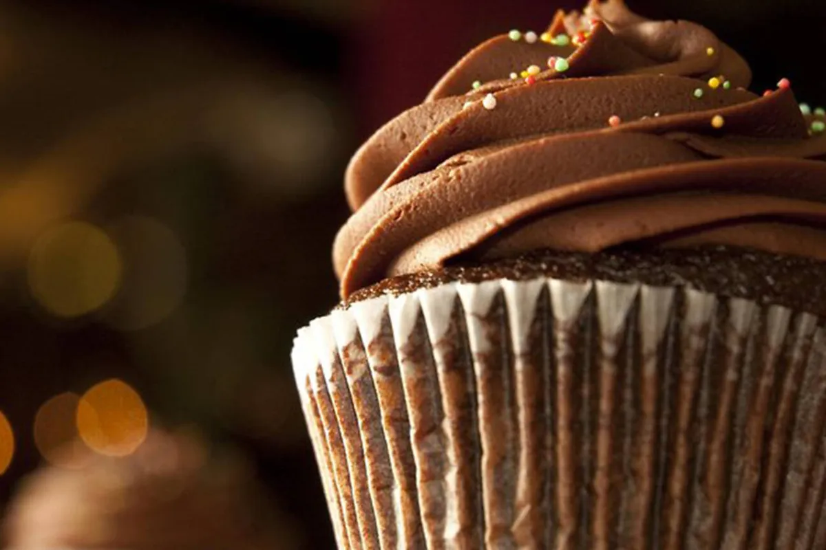 A frosted chocolate cupcake in a paper liner with sprinkles against a warm blurred background