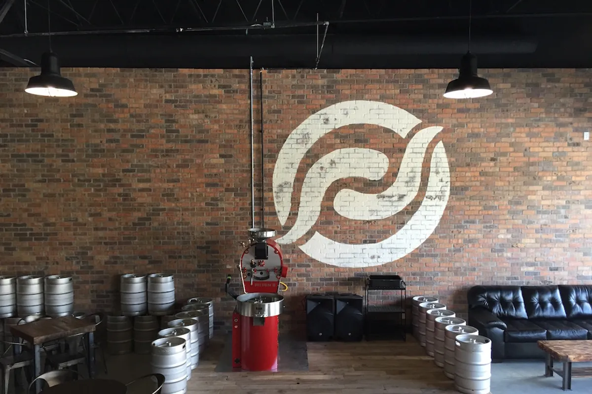 Red Horn taproom interior with logo on brick wall, red roaster on a wooden stage and stacked kegs