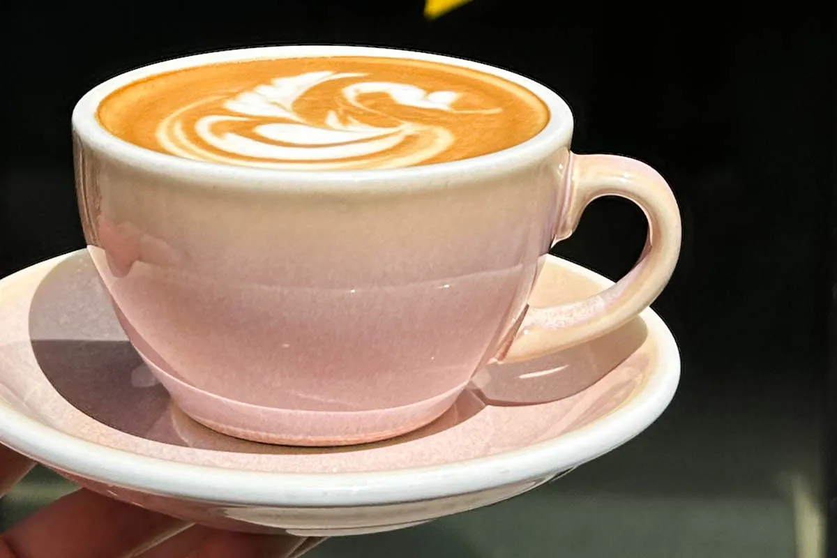 A pink cup of latte with swan-style latte art on a saucer, held before a black wall with a yellow star