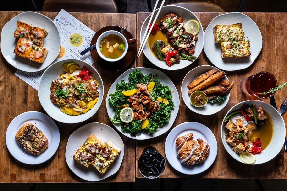 Overhead spread of toast, soups, salads and drinks on a wooden table at Sa-Ten Coffee & Eats