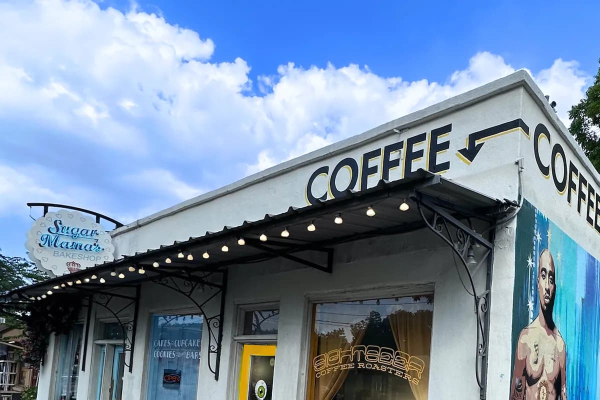 Whitewashed corner storefront with COFFEE lettering, string lights, yellow door, A-frame sign and a mural at right