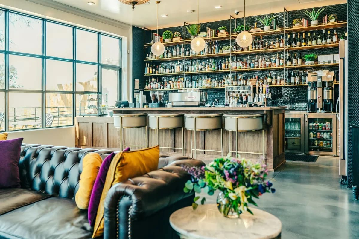 Simona bar with backlit bottle shelves, leather banquette with jewel-tone pillows and tall windows