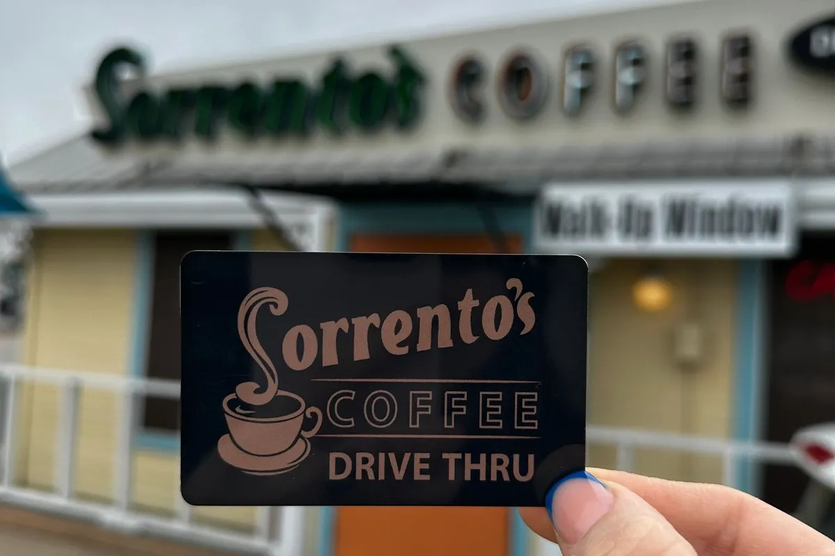 A hand holds a Sorrento Coffee Drive Thru card in front of the drive-thru building with walk-up window