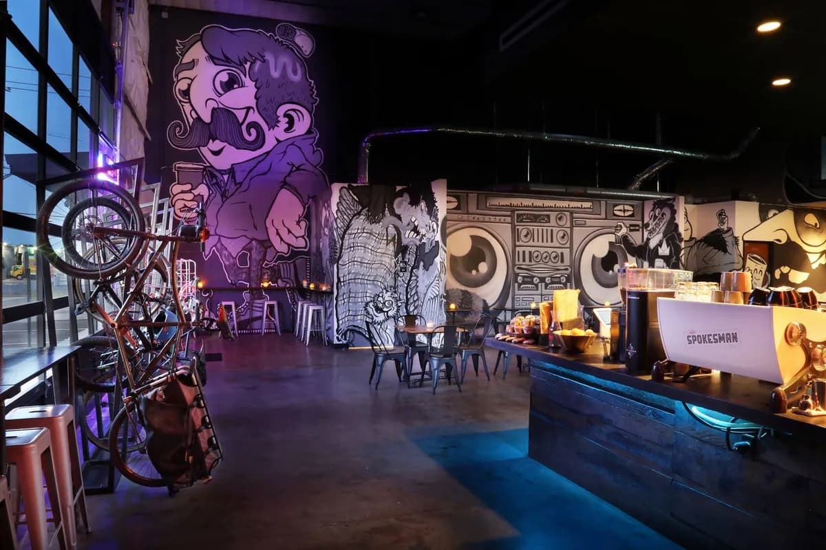 Warehouse cafe with giant mustachioed mural, bikes on the wall, tables, and the Spokesman-branded espresso machine on the bar