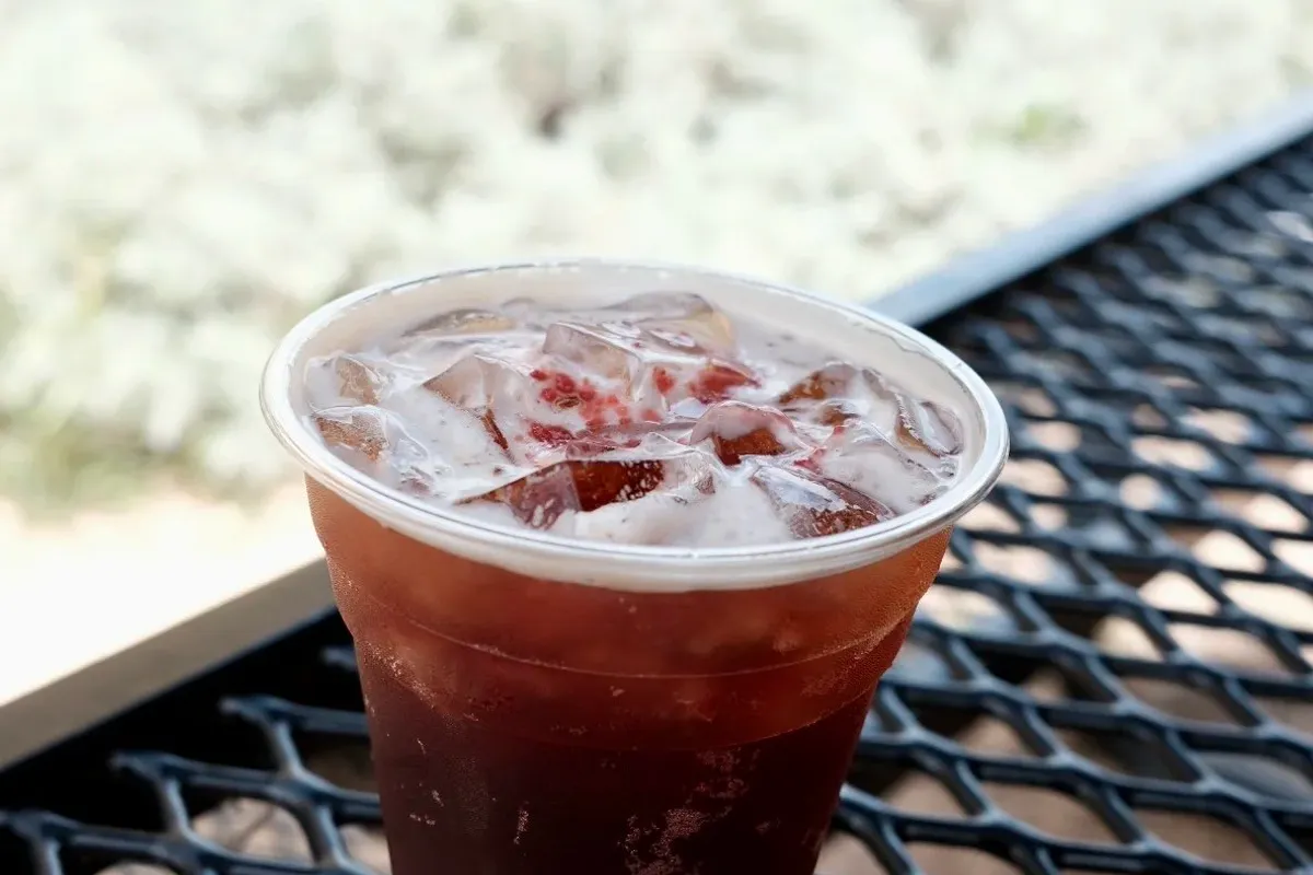 Iced red-tinged coffee drink in a clear cup on a black mesh patio table outdoors