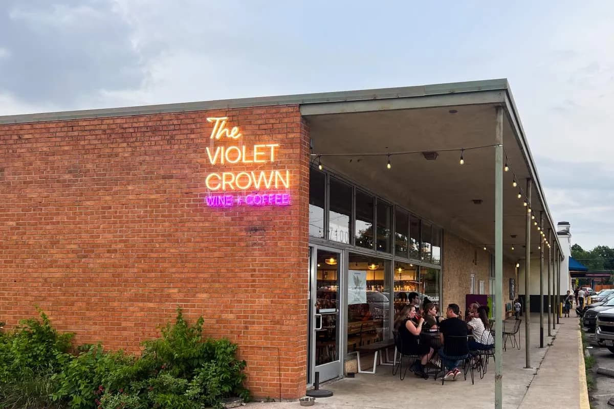 Brick storefront with neon Violet Crown Wine + Coffee sign and guests seated at patio tables under string lights