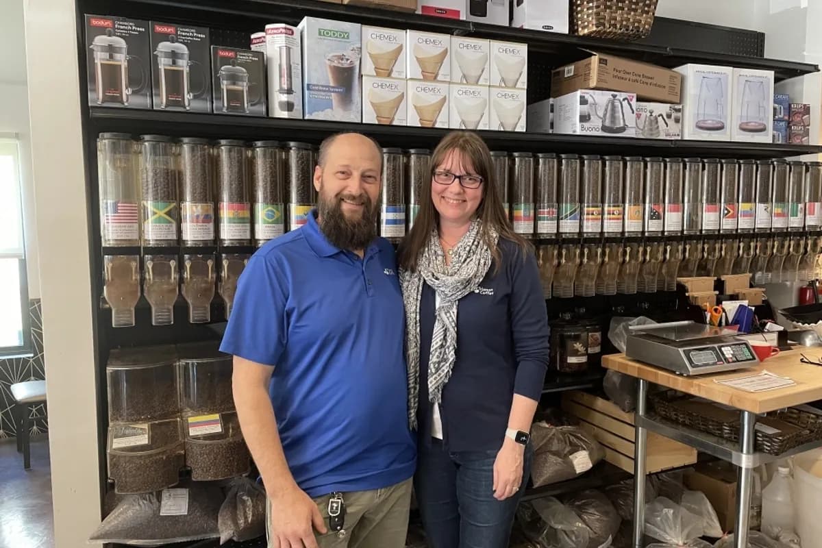 Two owners standing in front of shelves of bulk coffee bins and brewing gear inside the shop