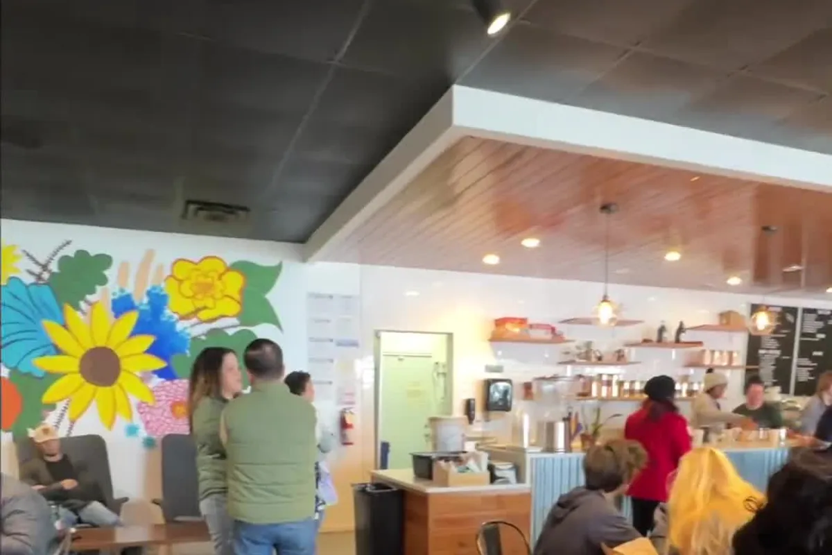 Cafe interior with colorful flower mural, seating, and customers near the counter