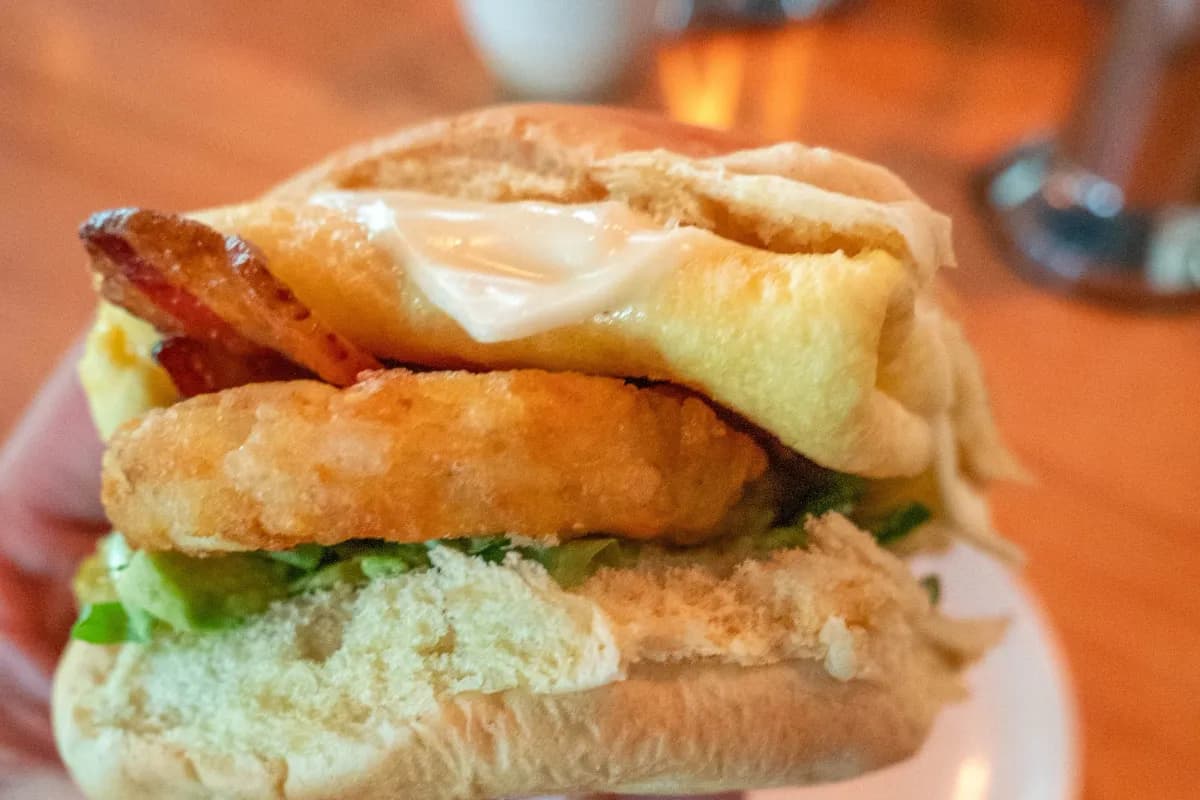 Hand holding a breakfast sandwich on a plate over a warm wood table